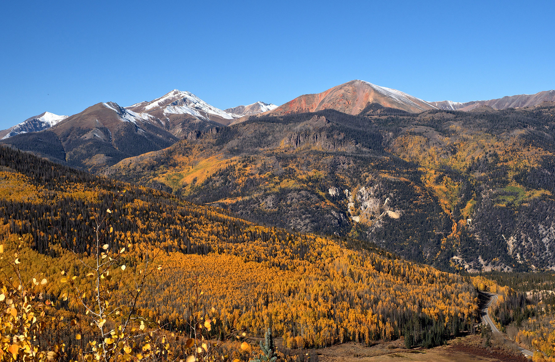 Southwest from Windy Point overlook is the edge of the Lake City Caldera on the right lower half of the field.  Red mountain (midright top) and Grassy mountain (midleft top) are also from middle-phase lava flows.  Igneous influx of metals (silver, gold) around the Lake City Caldera made it a very rich mining center.
