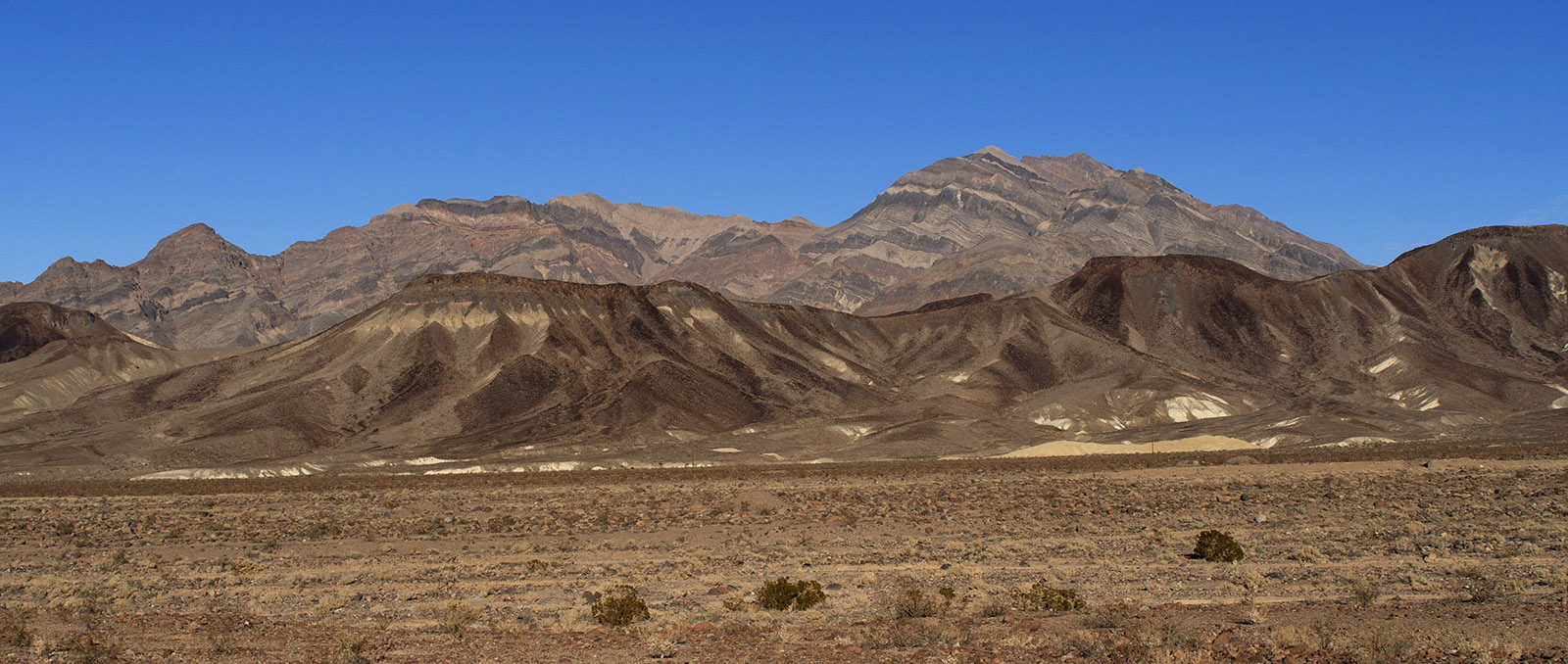 Funeral Mountains with Pyramid Peak in the background and Ryan Mesa (folded basalt deposited 4 MA in the Miocene Epoch) in the midground.  The Funeral Mountains are formed from Paleozoic sedimentary layers deposited in a shallow sea.  Layers have been folded and broken by thrust faults linked to Mesozoic compression and further tilted/cut by faults during the late Tertiary period.