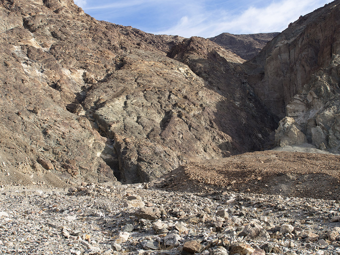 Badwater turtleback fault in shady area to the left separates the core Precambrian metamorphic rock in the turtleback on the left from tertiary sedimentary and igneous rock on the right.  Metamorphic rocks recovered from this area have been dated by radiometric methods at 1.7 billion years.