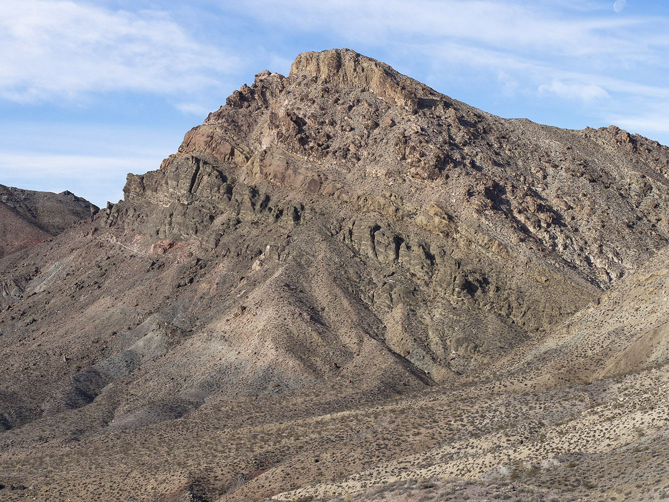 In this peak, slanted strata are Titus Canyon Formation strata from the Oligocene Epoch, Tertiary Period, 23-33 MA.  Titus Canyon Formation is composed of green conglomerate, red or green shale, sandstone and megabreccia deposits.  The top layer on the peak is volcanic rock deposited in the Miocene Epoch, late Tertiary Period, 22-20 MA.