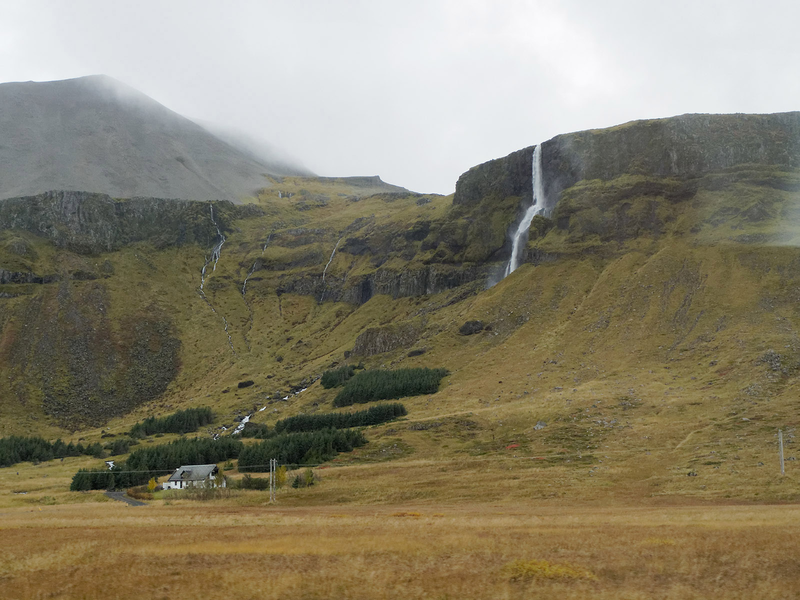 Farm house at the base of coastal cliffs and pasture on the coastal plain. The steep cliffs were once at the Atlantic coast line and have edges steepened by sea erosion over thousands and millions of years.  In post-ice age times (<25,000 years ago), the coastal plain was raised above sea level during the isostatic uplift of the Atlantic and the North American plate in the region.