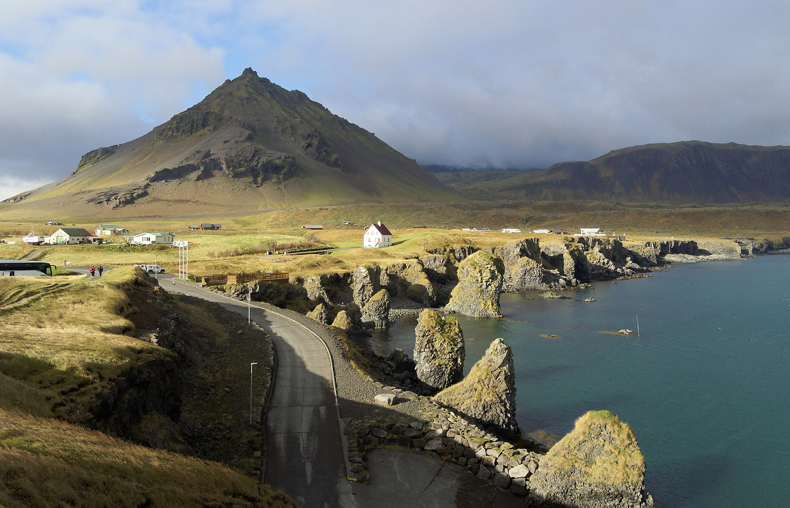 Eroding volcanic coastline near the village of Arnarstapi.  Multiple lava flows originating from Snæfellsjökull and related volcanoes in the Snæfellsnes Volcanic Belt have occurred in this area from 4,000 to 8,000 years ago, and older lava flows are also present in the region.  The cone-shaped volcano in the background (Stapafell) is a palagonitic pyramid volcano 526m high that is greater than 11,000 year old and less than 700,000 years old.