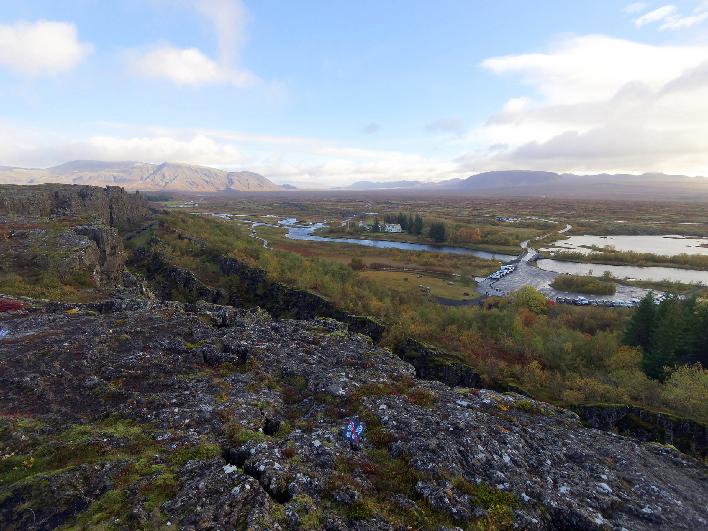 Þingvellir National Park Overlook at Almannagja (day 2) is at a rift valley on the crest of the Mid-Atlantic ridge. I’m standing on the North American plate which includes mountains on the left. Mountains on the far right are on the Eurasian tectonic plate. The sunken area with lakes and river in the center represents a graben where the surface drops as bordering tectonic plates are pulled apart. Large faults including Almannagja are on the left side of the valley.
