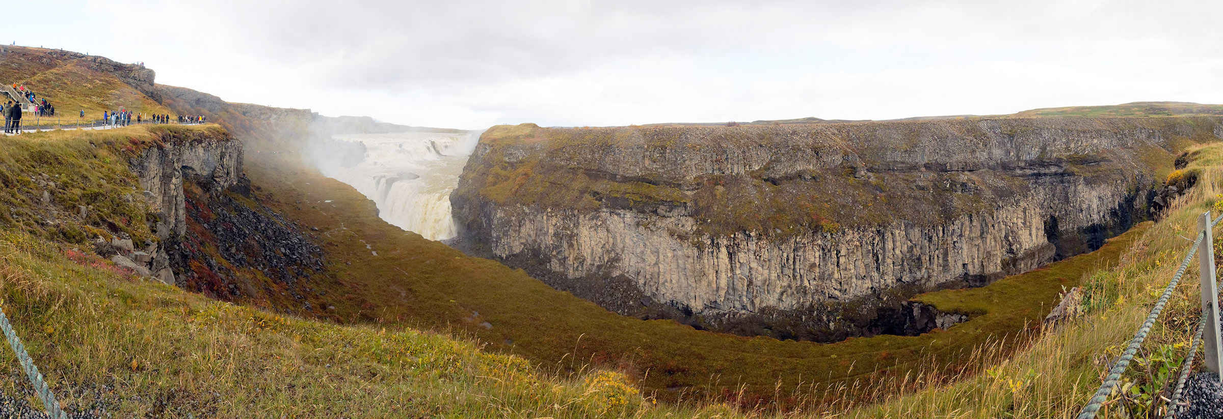 Gullfoss (Golden Falls) panorama including the falls and the downstream gorge/canyon cut by the Hvítá river. The river water originates from glacial, spring and rain run-off and have an average flow of 110 cubic meters per second. The panorama lines up the three strata layers with the step levels of the falls. 
Watch the video of the falls on the Iceland tour main web page.