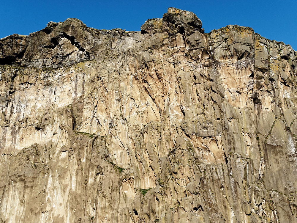 Steep cliffs of hyaloclastites containing red oxidized iron on Heimaklettur (the largest mountain) at the entry of the main harbor of Vestmannaeyjabaer on the island of Heimaey. Heimaey, the largest of the Westman islands, formed between 5,200 and 6,000 years ago.  The cliffs are mainly hyaloclastites formed under glaciers or under sea where lava extrusion is rapidly cooled by ice and water to produce large glass-like crystals.