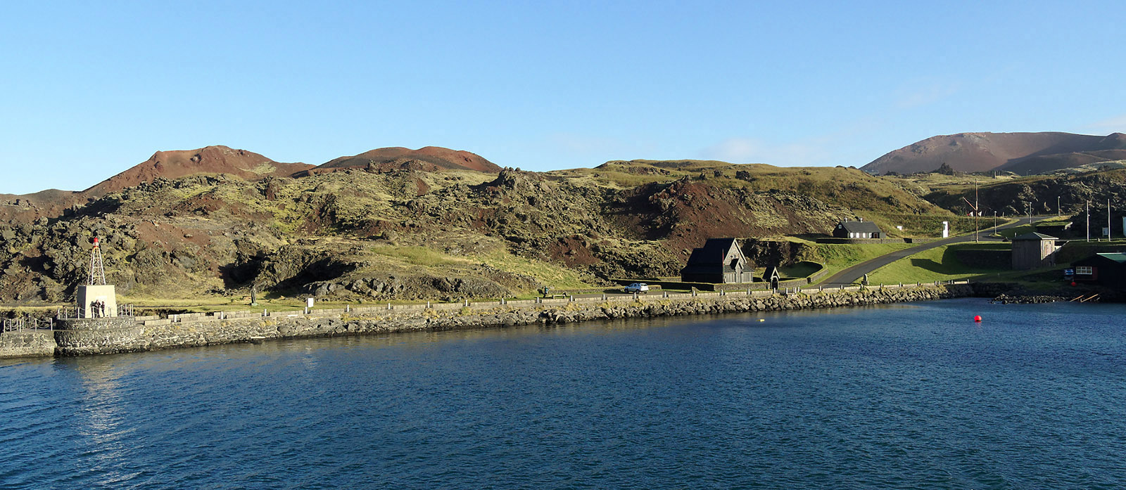 New fields of lava and tephra that extend to the north and west from Eldfell into the harbor are bordered by new structures (e.g., Stafkirkjan – Norwegian stave church). During the eruption, high-volume water pumps shot water onto the lava flow to make cooled walls/damns to divert the lava flow so that the harbor would not be completely blocked.